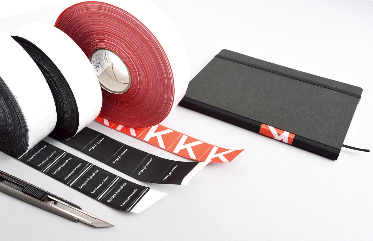 Produktion von Notizbüchern: Bandmaterial, Etiketten und Hardcover-Buch auf Arbeitstisch
