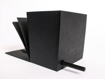 Notizzettel Cube, schwarzer Zettelblock mit Stift, aufgefächerte Notizzettel im Hintergrund